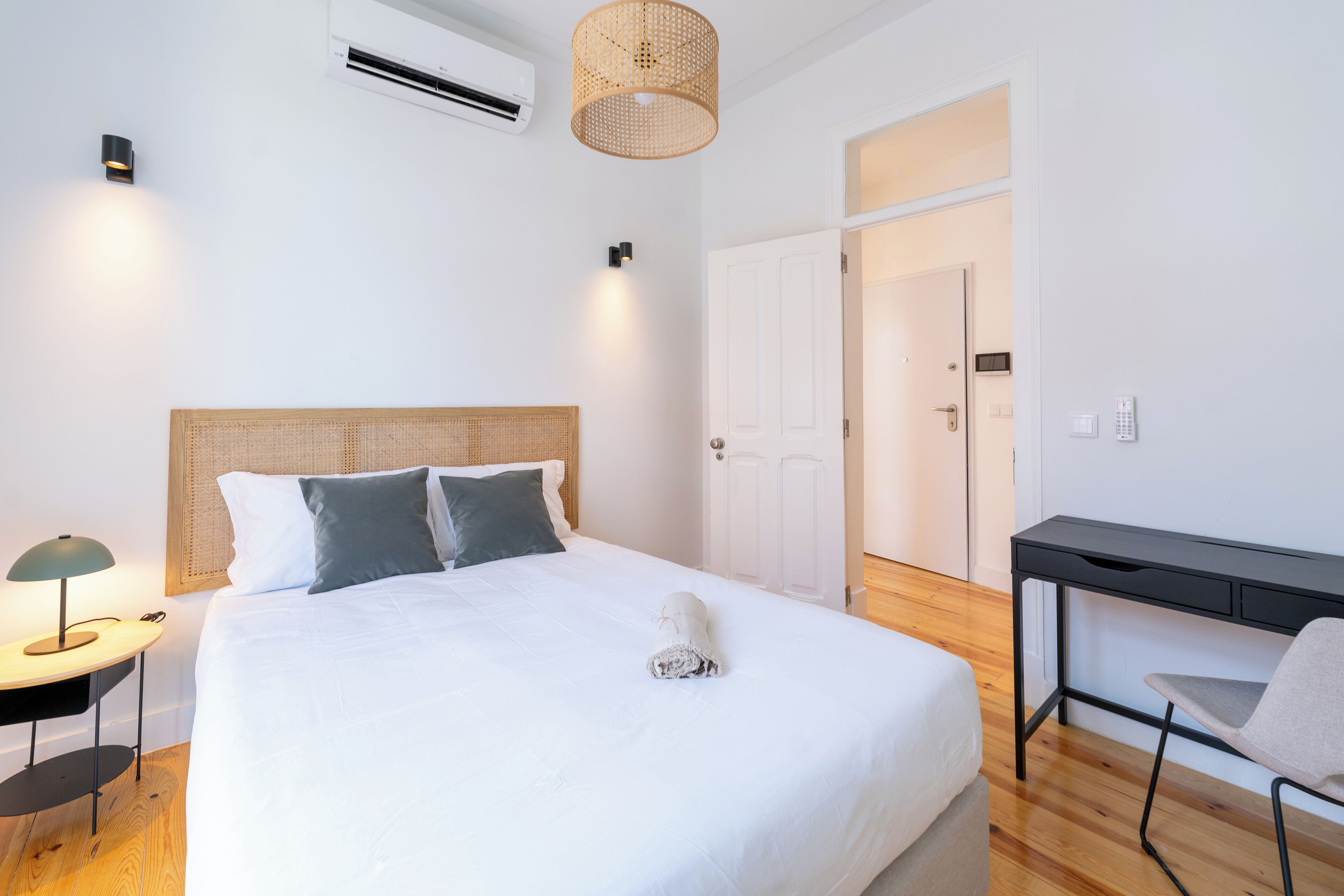 A neatly arranged bedroom with a bed, bedside table, lamp, and a desk with a chair.