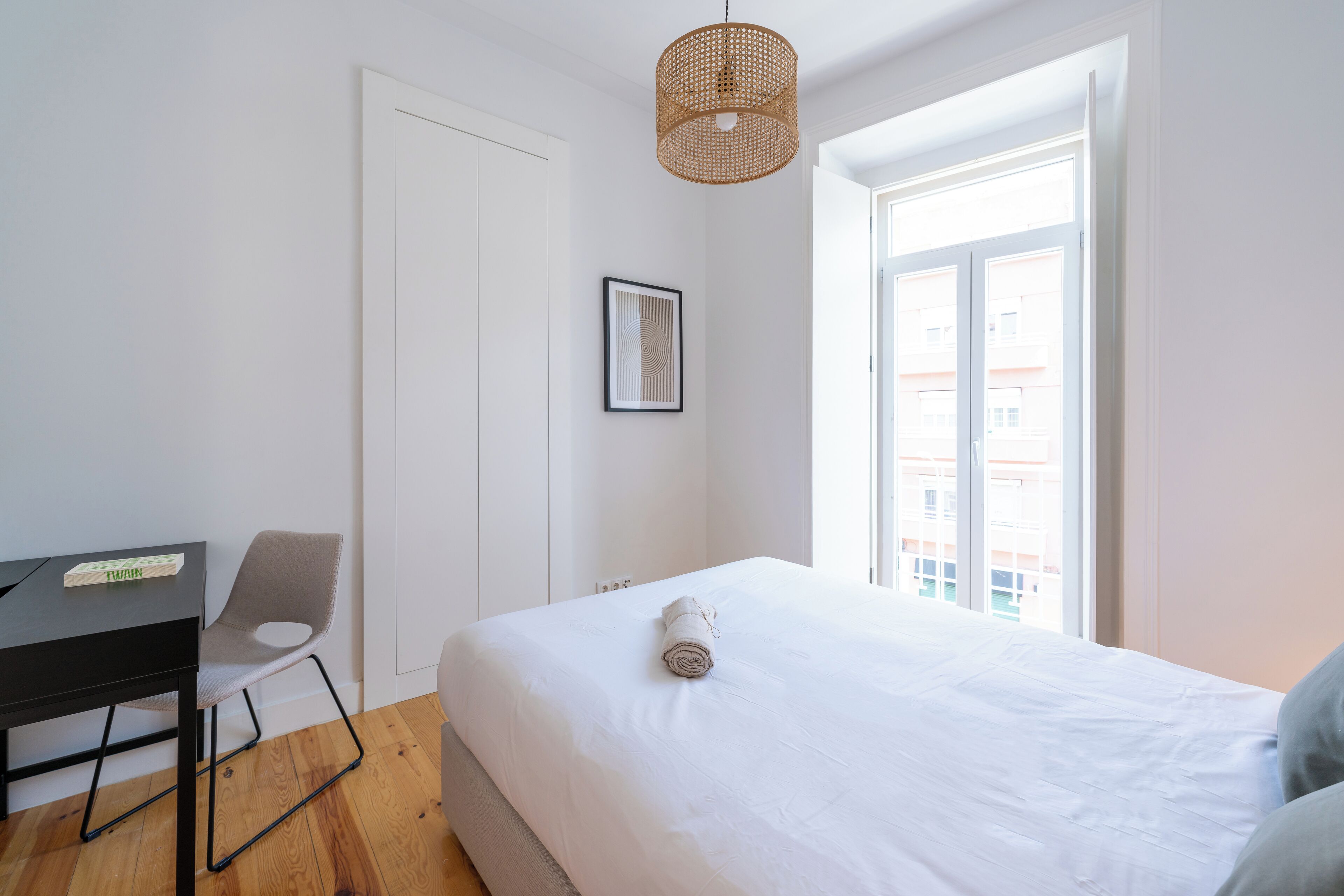 Une chambre à coucher comprenant un lit, un bureau, une chaise, une porte, une fenêtre et un luminaire suspendu.