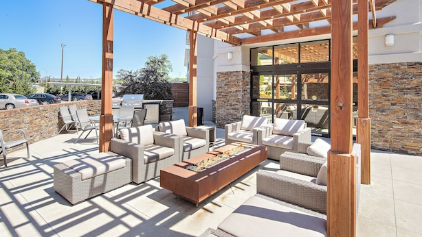 Een terras buiten met rieten meubilair, een vuurkuil en een pergola.