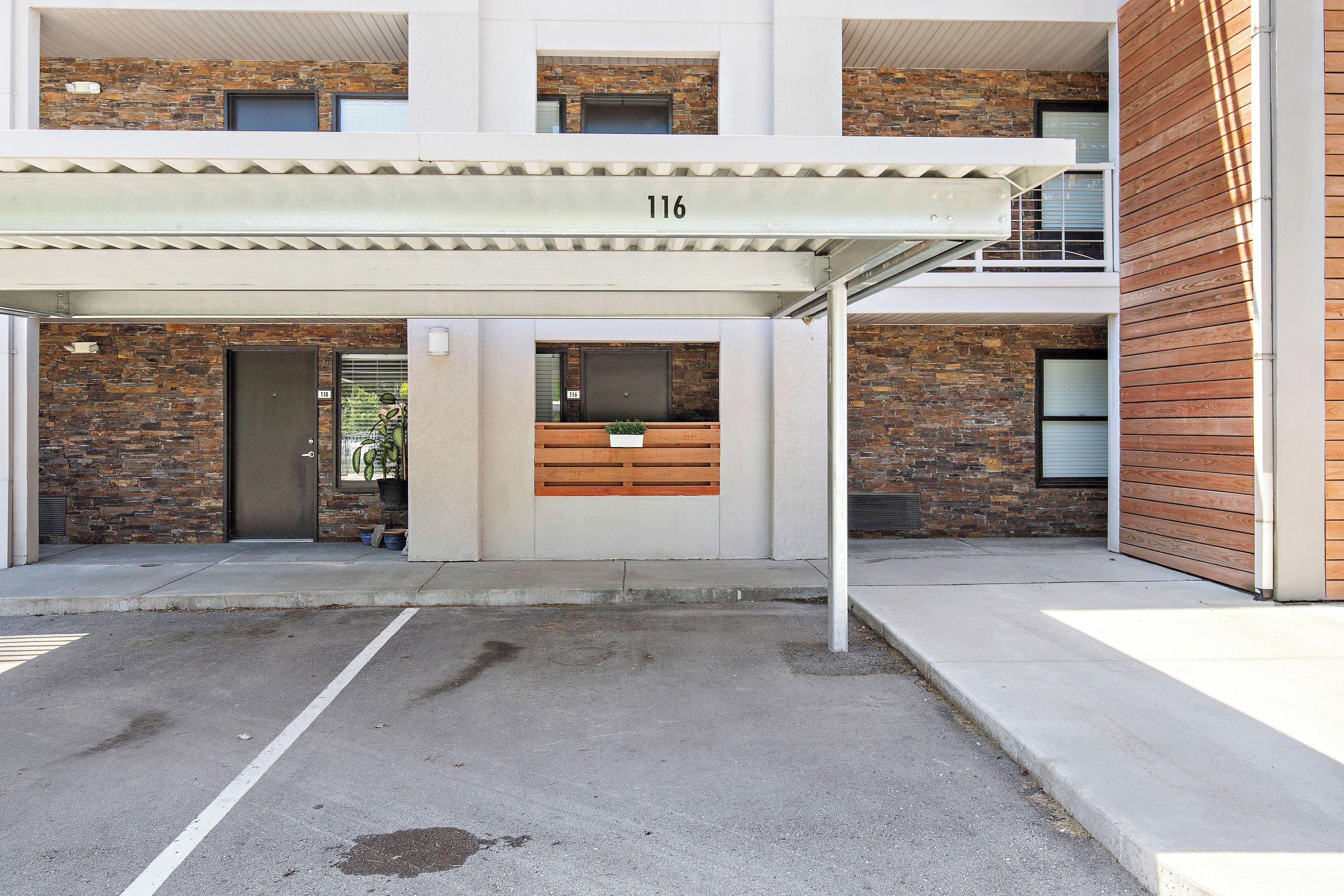 A modern building with a brick facade, numbered 116, featuring a covered entrance, a wooden bench, and a small planter.
