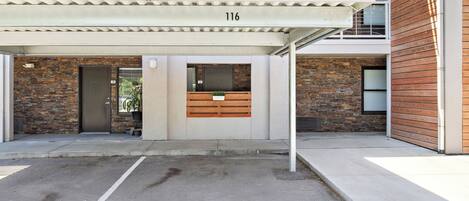 A modern building with a brick facade, numbered 116, featuring a covered entrance, a wooden bench, and a small planter.