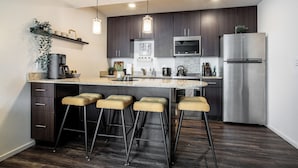 Een moderne keuken met donkere houtkasten, roestvrijstalen apparatuur, een centraal eiland met barstoelen, hanglampen en een inbouwoven.