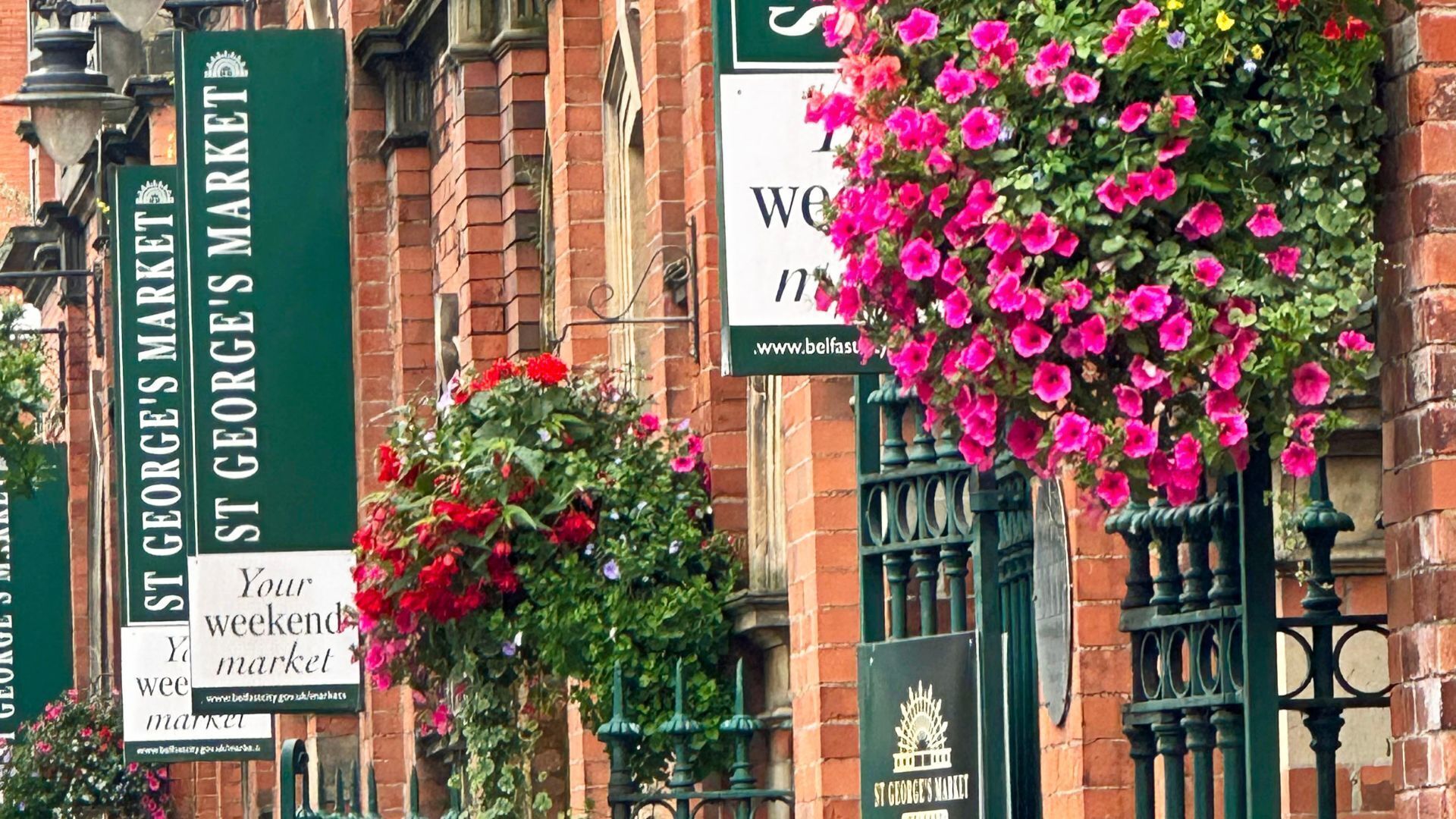 Um edifício de tijolos com placas indicando o St George's Market, incluindo uma placa com a inscrição 'You Weekends Market'.