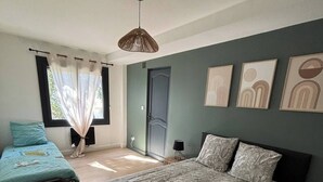 Un dormitorio con una cama grande, una cama más pequeña, una ventana con cortinas y decoración en la pared.