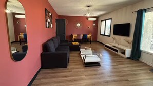 Una sala moderna con un sofá modular, un televisor de pantalla plana y una zona de comedor con manteles amarillos.