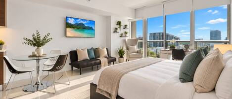 Une chambre moderne avec un grand lit, un canapé, une table à manger et des chaises. Une grande fenêtre offre une vue sur la ville.