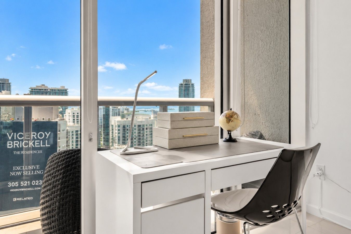 Ein moderner Schreibtisch mit Globus, Lampe und Stuhl in einem Hochhaus mit Blick auf die Stadt.
