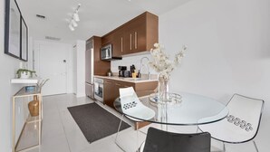 A modern kitchen with brown cabinets, a white countertop, and a dining area with a glass table and chairs.