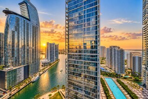 A high-rise building with a glass facade, a waterfront promenade, and a pool area.