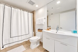 A modern bathroom with a white toilet, a large mirror, a white sink, and a shower curtain.