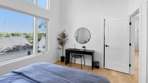 A bedroom with a bed, a desk, a chair, a potted plant, a mirror, and a door. - Modern suite | Mins from DT Raleigh | Workspace (Raleigh)