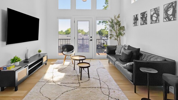 A modern living room with a flat-screen TV, a sofa, a coffee table, and a large window with a view of a balcony. - Modern suite | Mins from DT Raleigh | Workspace (Raleigh)