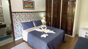 A neatly made bed with a blue bedspread and pillows, a heart-shaped towel arrangement, a framed sign on the wall, and a wooden wardrobe.