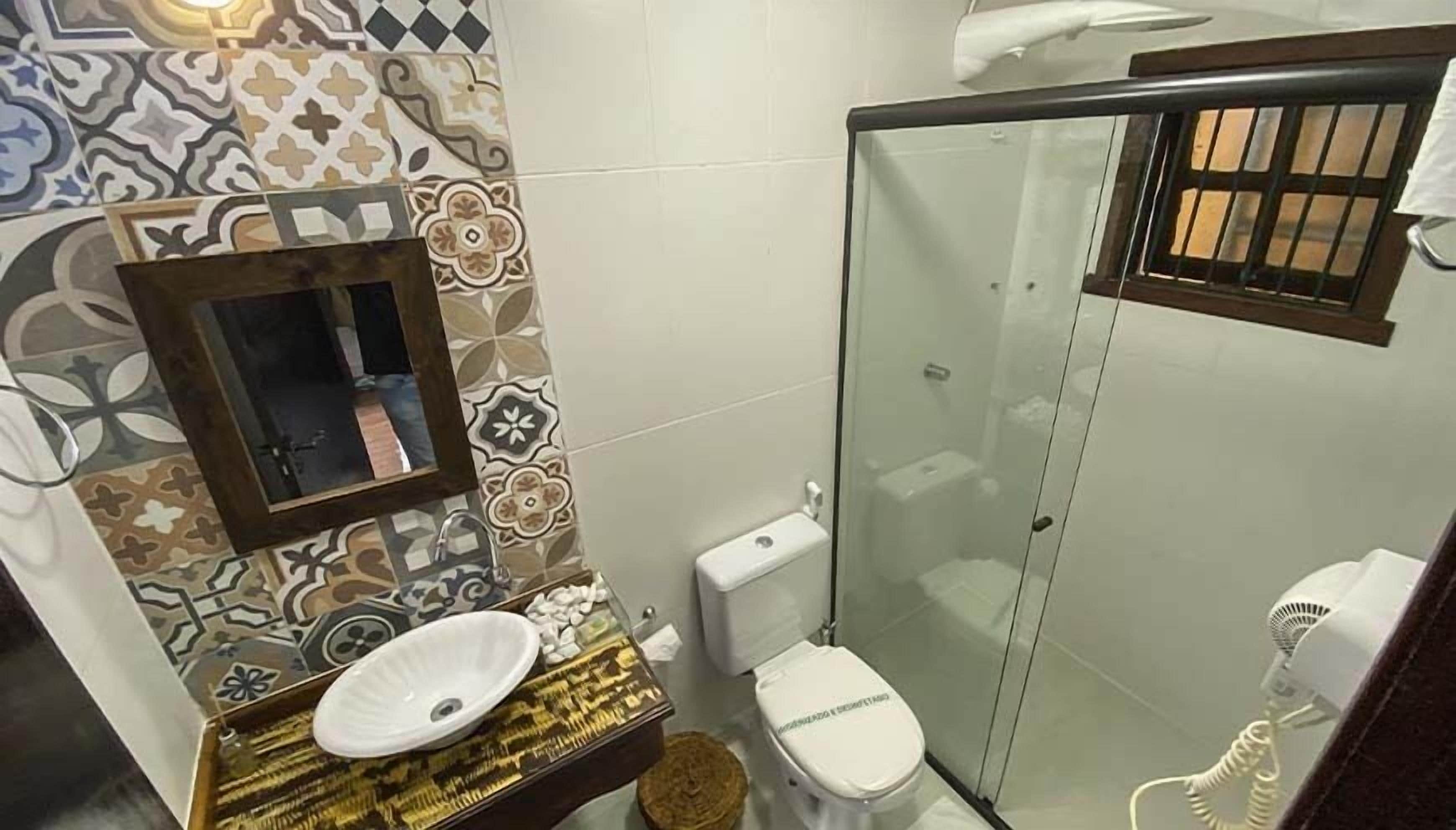 A bathroom with a patterned tile wall, a sink, toilet, and a glass-enclosed shower.