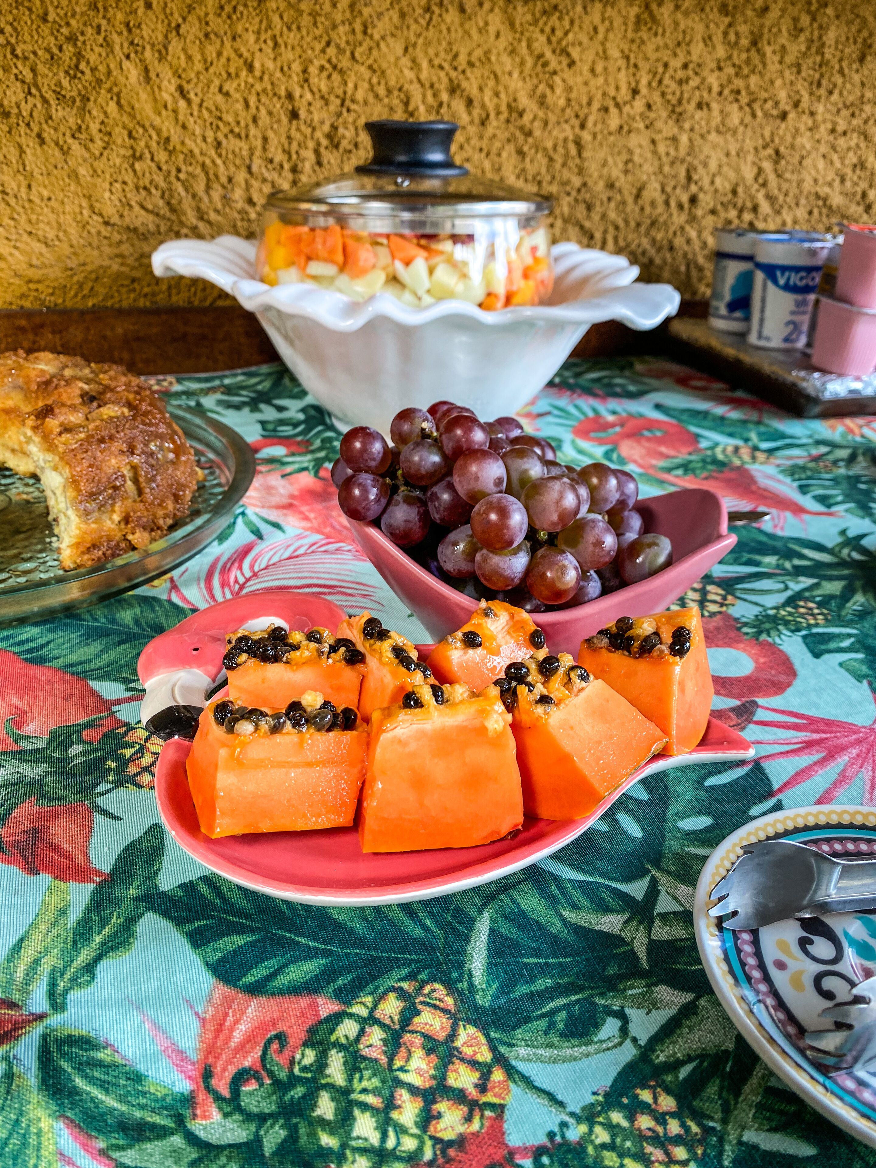 A table with a fruit platter, a bowl of grapes, and a covered dish with a dessert.