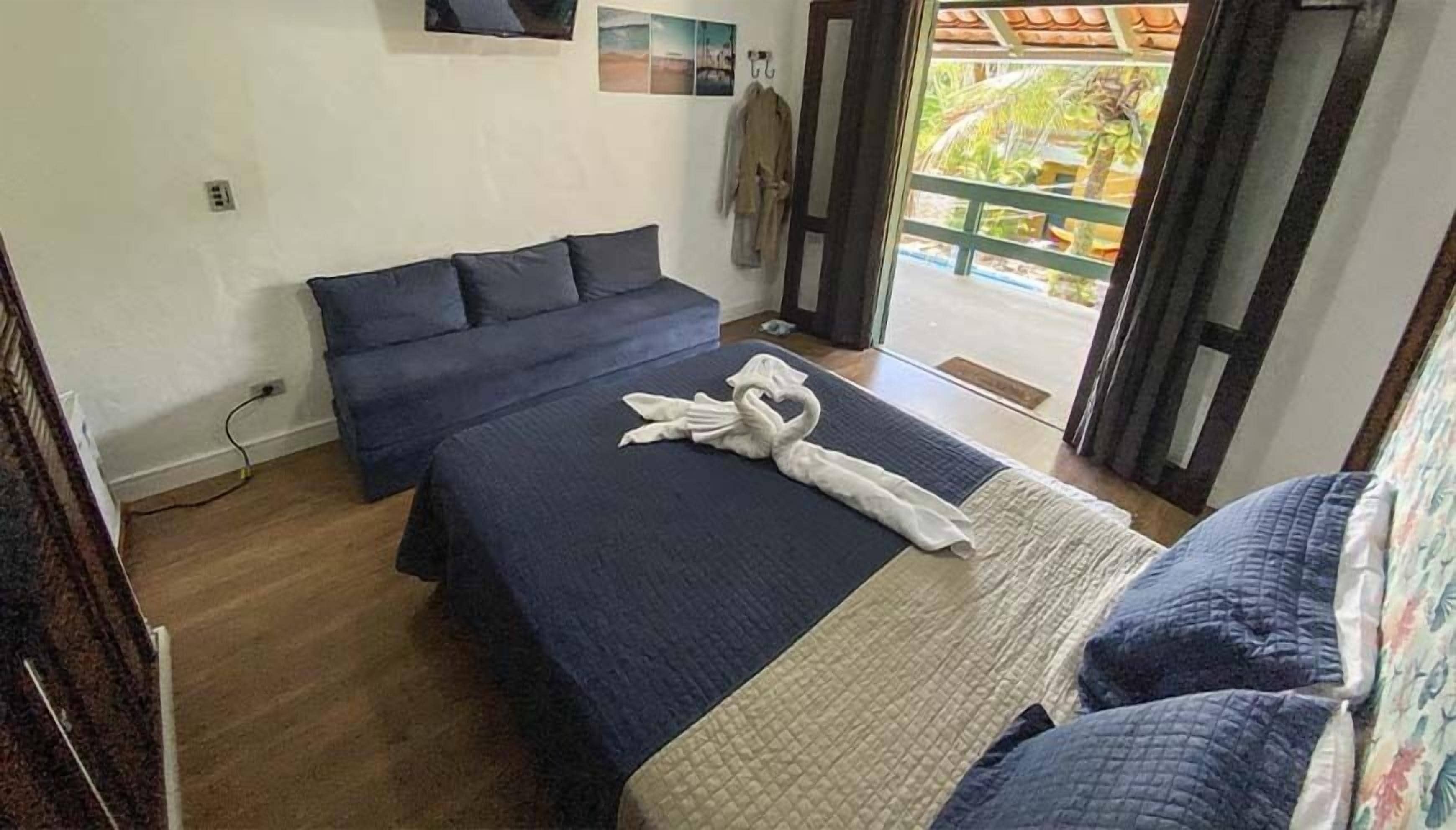A bedroom with a bed, a sofa, a towel art, and a view of the outdoors.