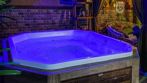 Een hottub met houten frame, omgeven door een bakstenen muur en een houten afdak.