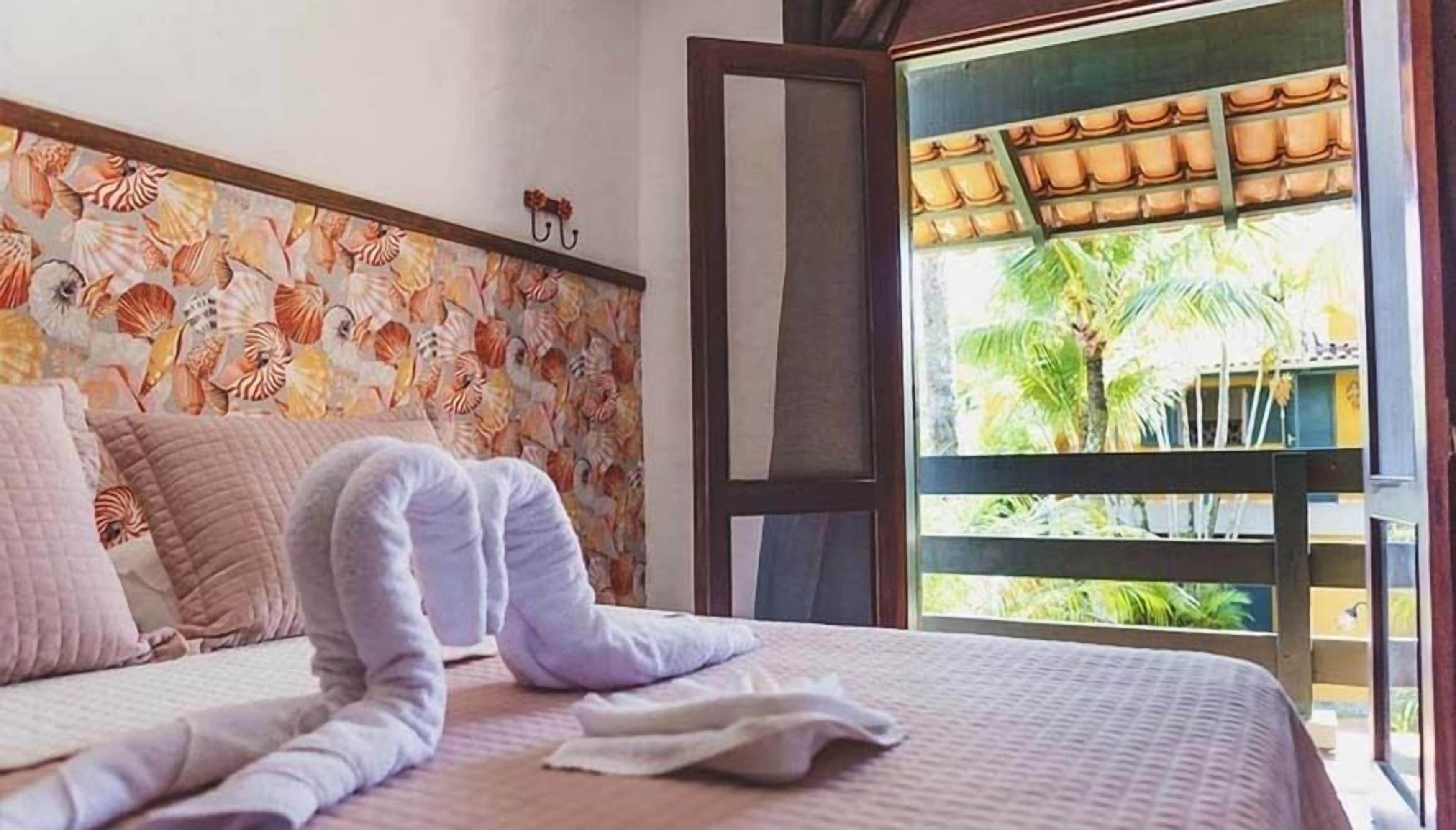 Quarto com uma cama, parede decorativa e vista para palmeiras.