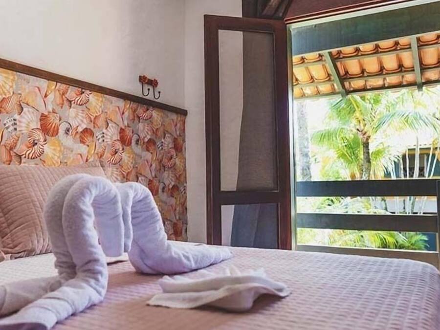 Quarto com uma cama, parede decorativa e vista para palmeiras.