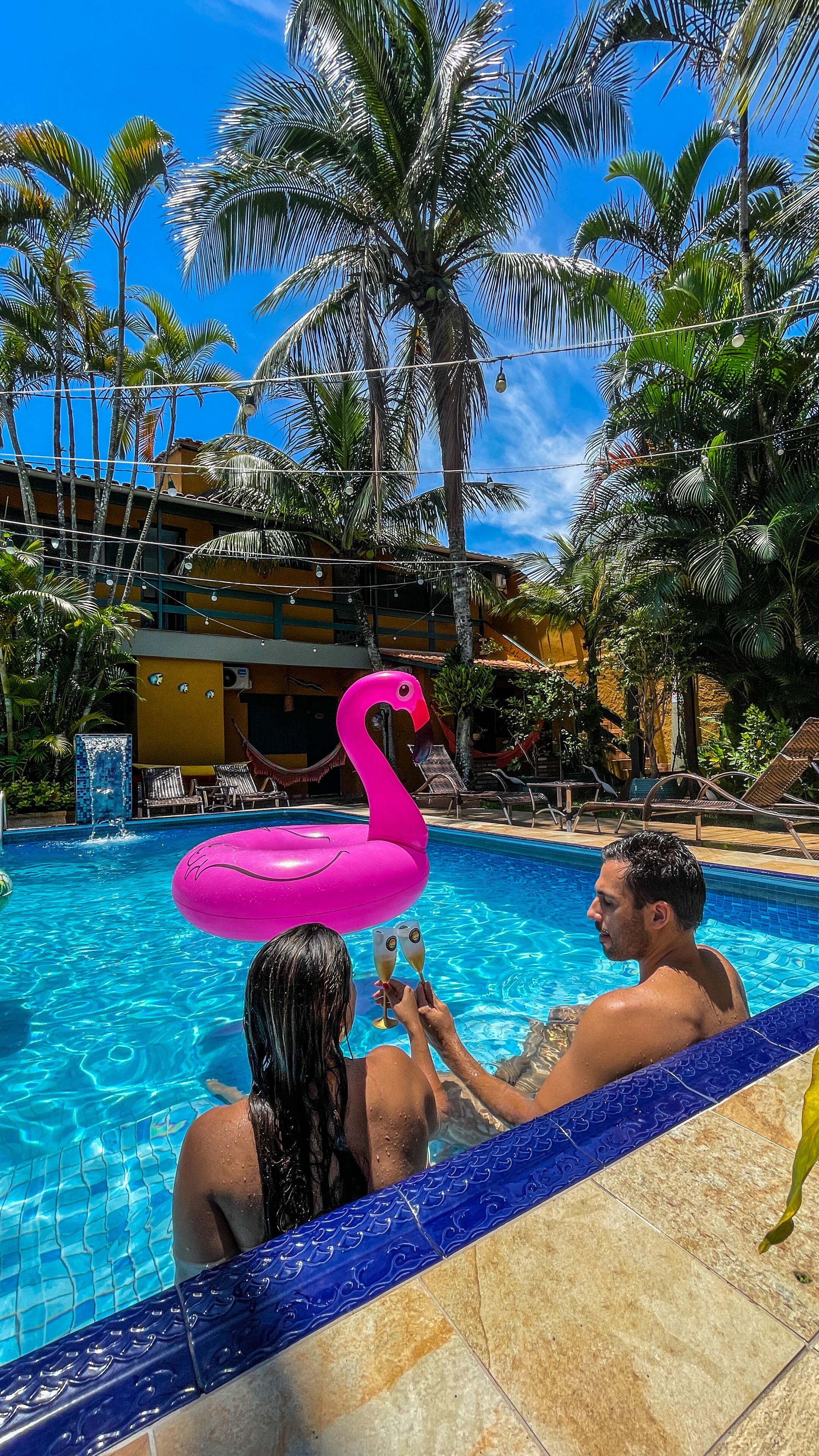 A swimming pool with a pink flamingo float, lounge chairs, and palm trees.