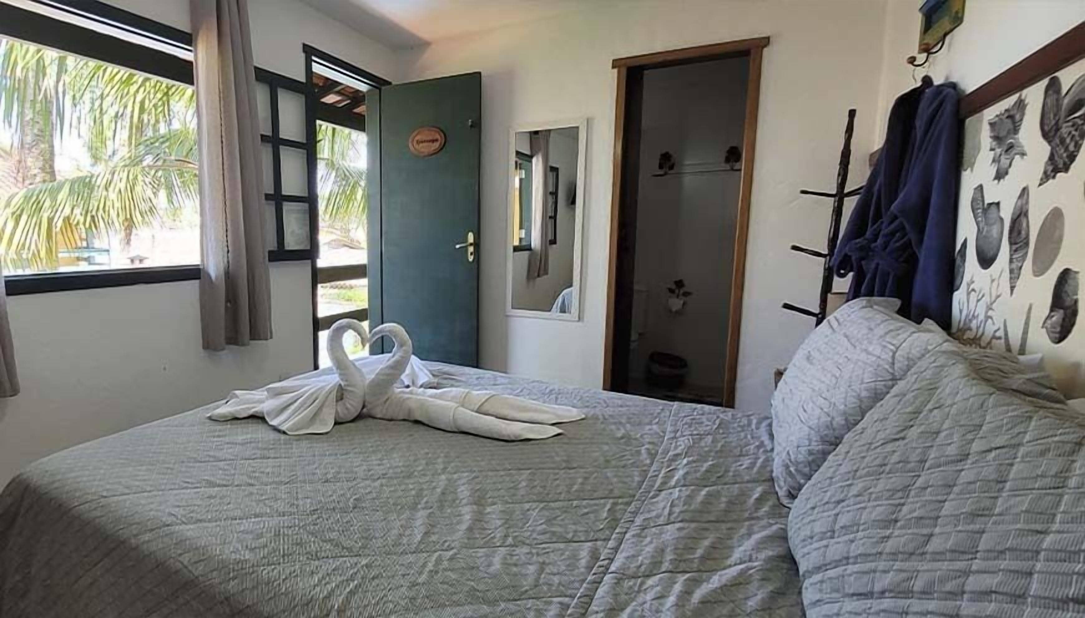 A bedroom with a bed, a window with curtains, a door, and a wall with a mirror and wall art.