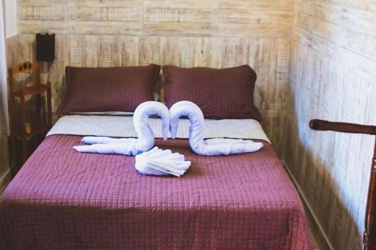 Un lit recouvert d’une couvre-lit violette et orné de deux oreillers, une chaise en bois et un mur dont le revêtement présente un motif texturé.