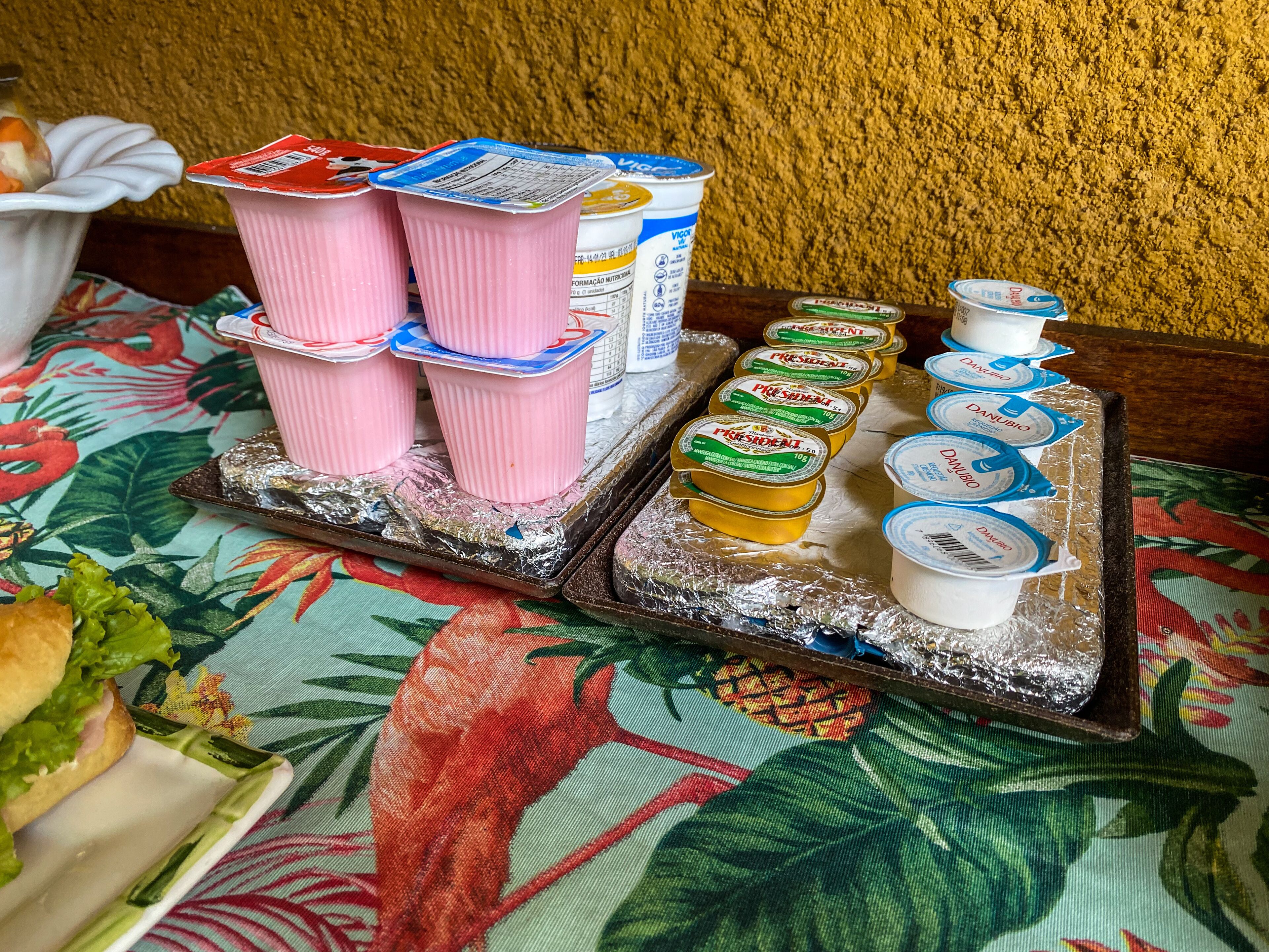 A tray of food items including yogurt cups and containers, placed on a table with a floral tablecloth.