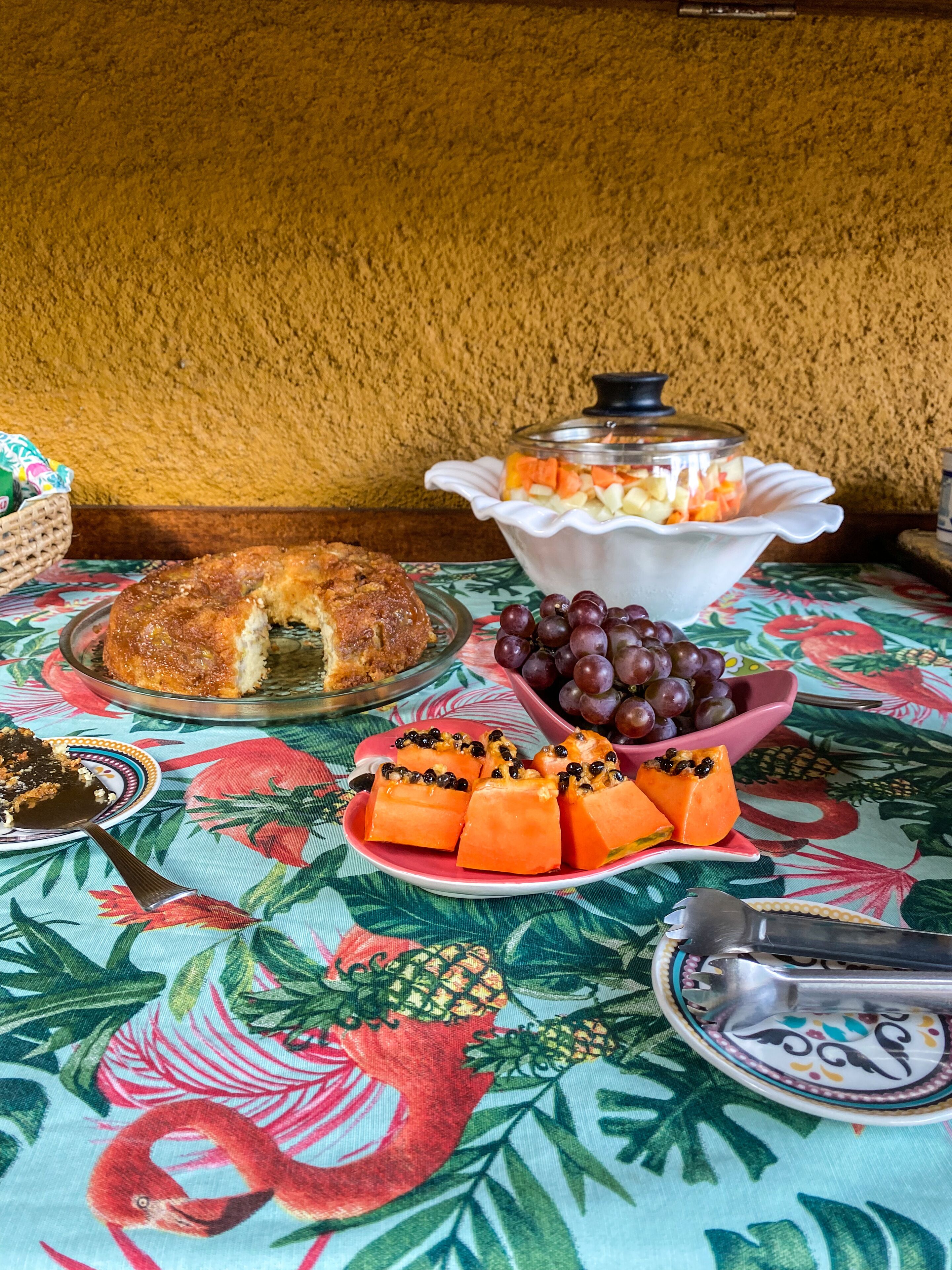 Una mesa con una bandeja de fruta, un pastel y un bol de uvas.