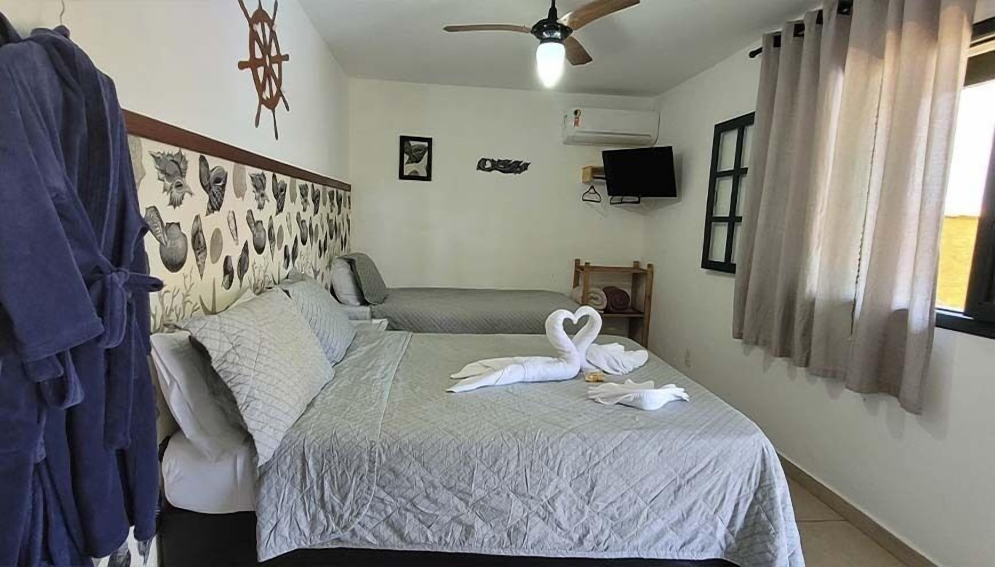 A hotel room with a bed, a robe rack, a ceiling fan, a wall-mounted TV, and a window with curtains.