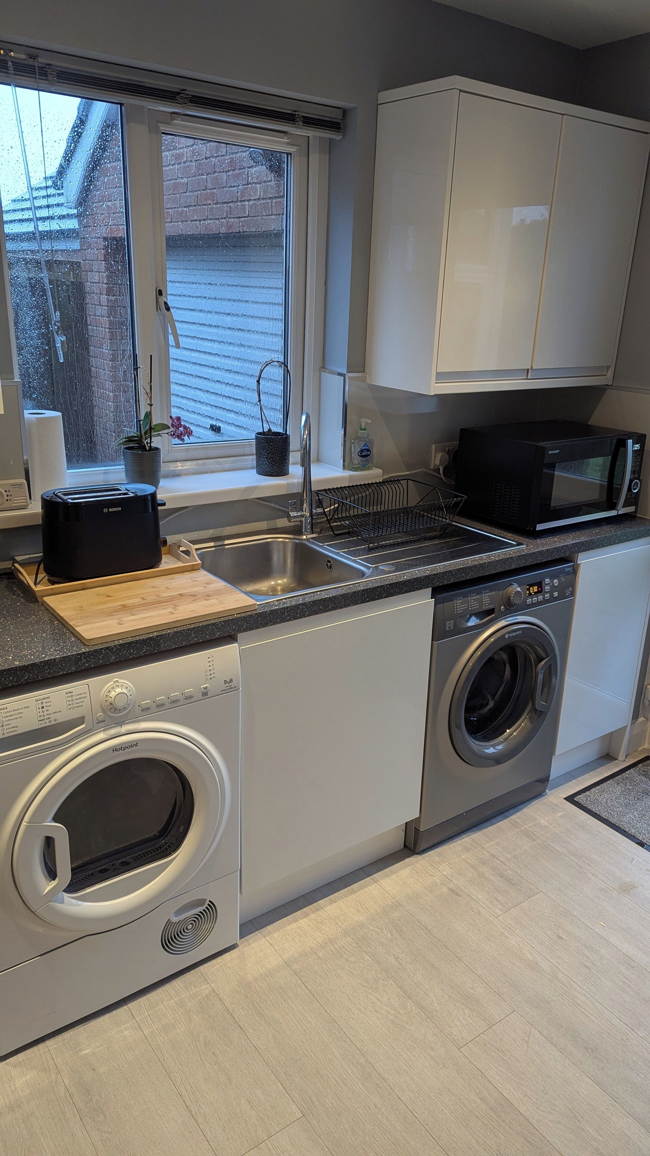 A compact kitchen with a Bosch toaster, a microwave, a washing machine, and a dish rack.