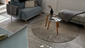 Een moderne woonkamer met een grijze bank, een ronde glazen salontafel en een grijs vloerkleed.