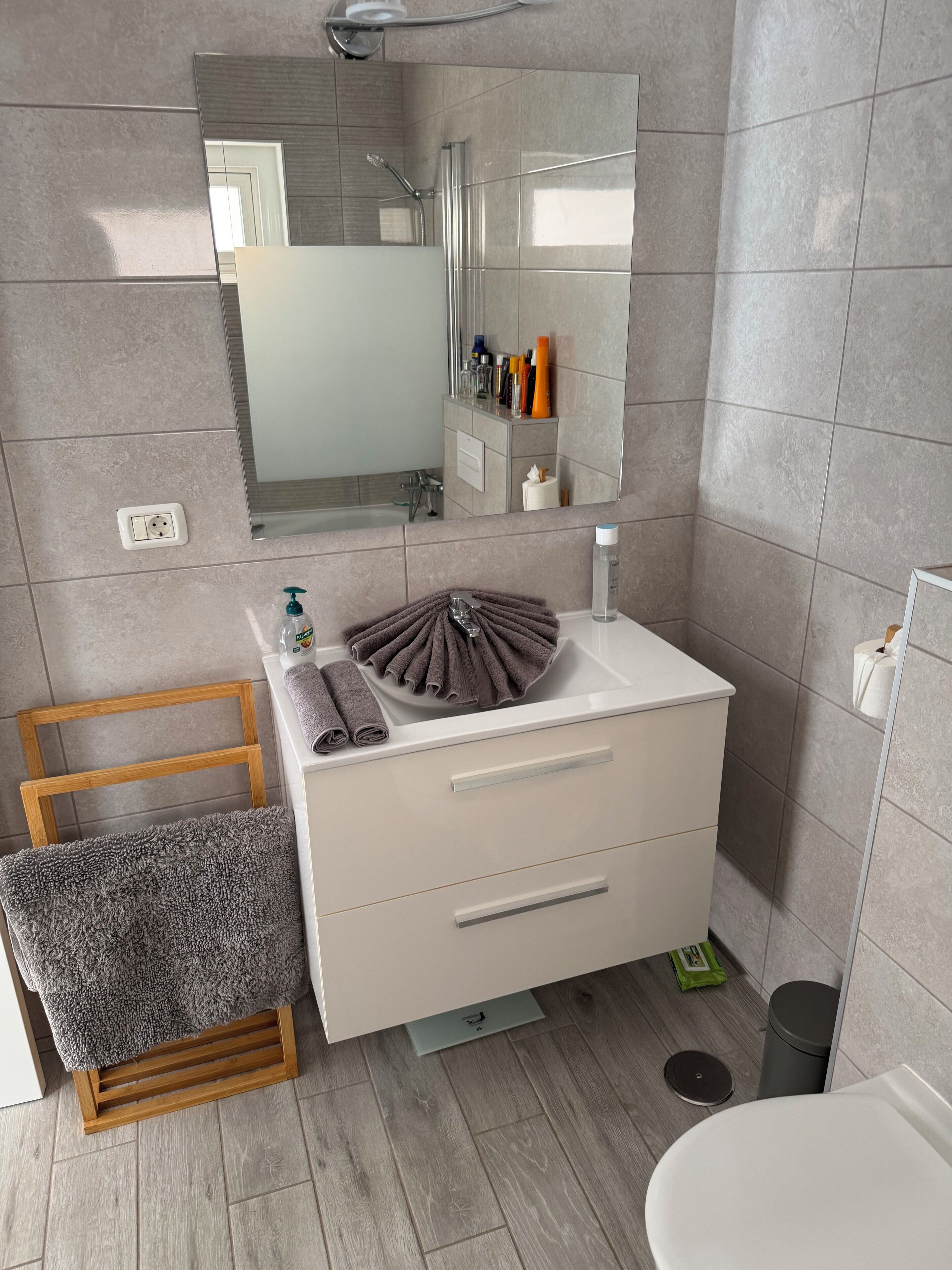 A modern bathroom with a wooden chair, a sink with a towel holder, and a mirror above the sink.