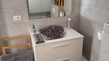 A modern bathroom with a wooden chair, a sink with a towel holder, and a mirror above the sink.