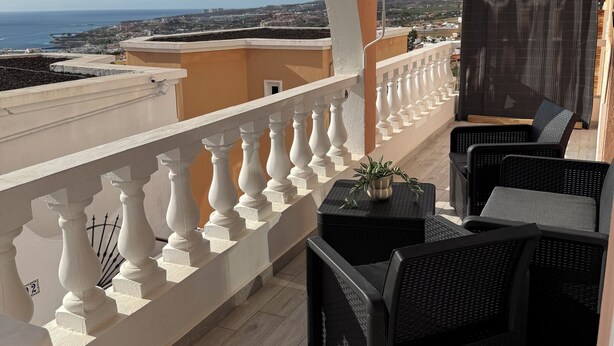 Een balkon met witte leuningen, rieten meubels en een plant in pot.