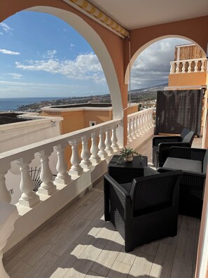 A balcony with white balustrades, wicker furniture, and a potted plant. - Modern vacation suite with sea view (Costa Adeje)