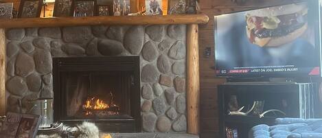 A rustic cabin interior with a stone fireplace, wooden walls, and deer antlers mounted on the wall.