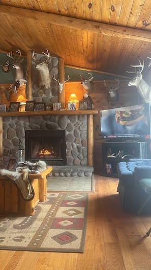 A rustic cabin interior with a stone fireplace, wooden walls, and deer antlers mounted on the wall.