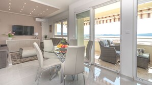A modern living room with a glass dining table, comfortable seating, a flat-screen TV, and a balcony with a view.