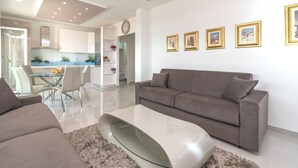 A modern living room with a grey sofa, a glass coffee table, and a dining area with a glass table and chairs.