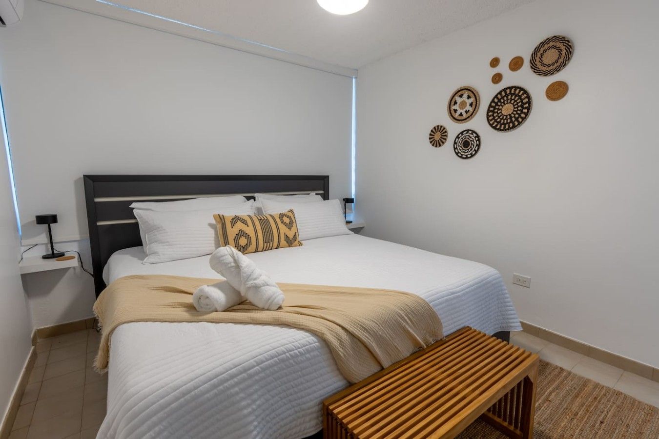 Una cama bien hecha con ropa blanca, un banco de madera y decoración en la pared.