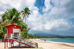 A beach with a lifeguard station, palm trees, and a clear sky. - Beach Apartment in Río Grande (Villa Quenepa) (Rio Grande)