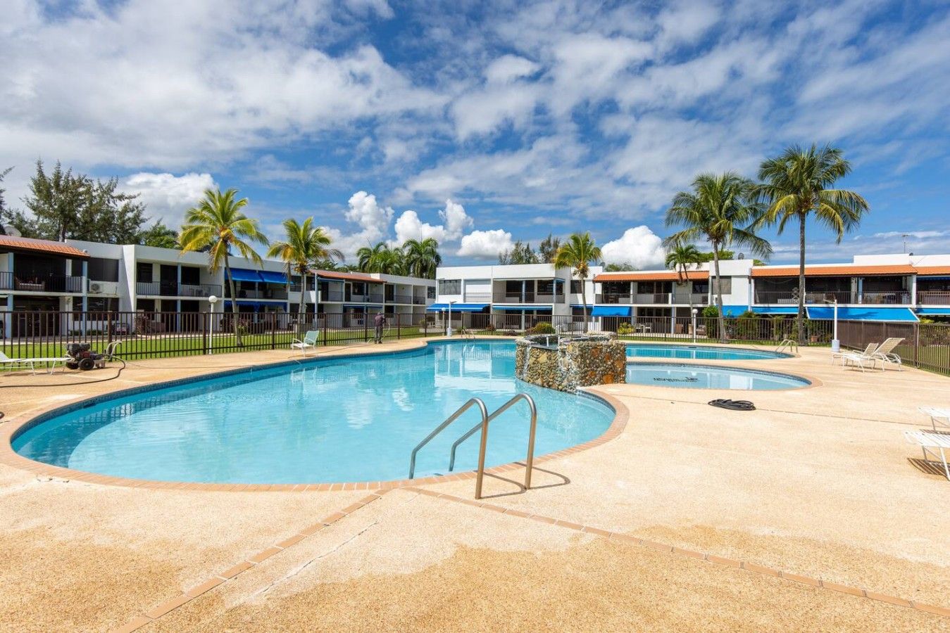 Área de piscina em resort, com várias piscinas, espreguiçadeiras e palmeiras.