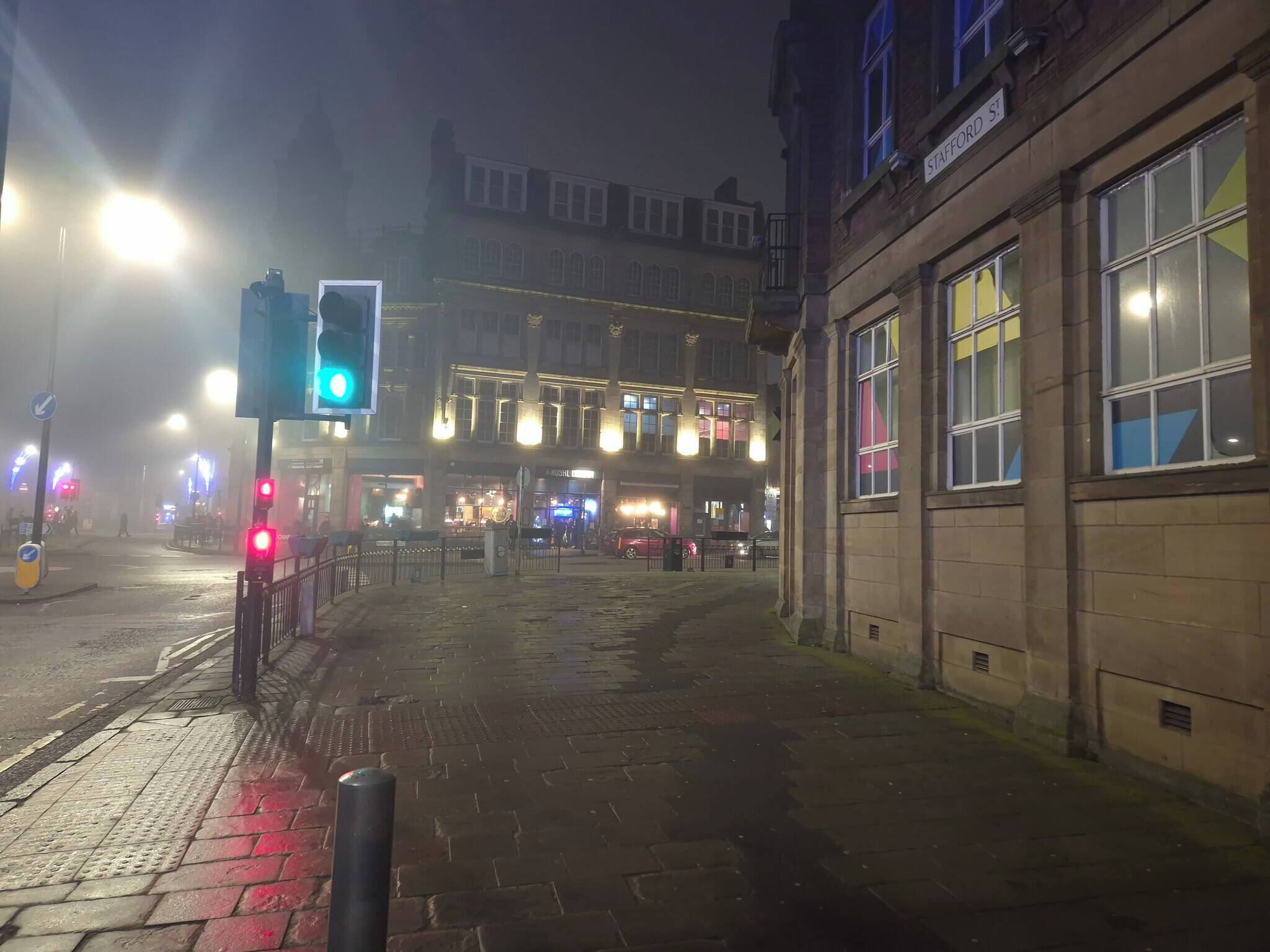 A nighttime street scene with a traffic light displaying green, a pedestrian crossing, and a building with a sign reading "Stafford St."