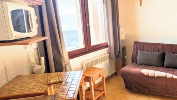 A compact kitchen with a microwave, wooden table, and a sofa in a cozy room. - Bright 14m2 studio with unobstructed view (Saint-Michel-de-Chaillol)