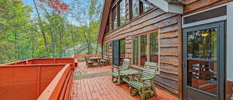 A wooden cabin with a deck, large windows, and a view of the surrounding forest.