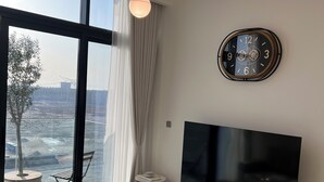 A modern living room with a large TV, a sofa, a small table, and a view of a construction site through large windows. - Luxury 1BDwith Stunning Burj Khalifa View- Self Check-in (Dubai)