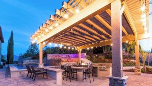 Un patio exterior con pérgola, mobiliario y zona de barbacoa.