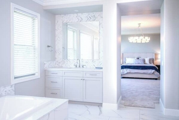 A modern bedroom with a large bed, a walk-in closet, and a bathroom with a vanity and sink.