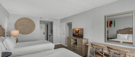 Two large beds with crisp white linens, a desk with chair, and a mounted TV.