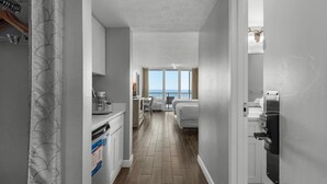 Un pasillo estrecho con una zona de cocina a la izquierda, un comedor en el centro y un dormitorio con ventana a la derecha.